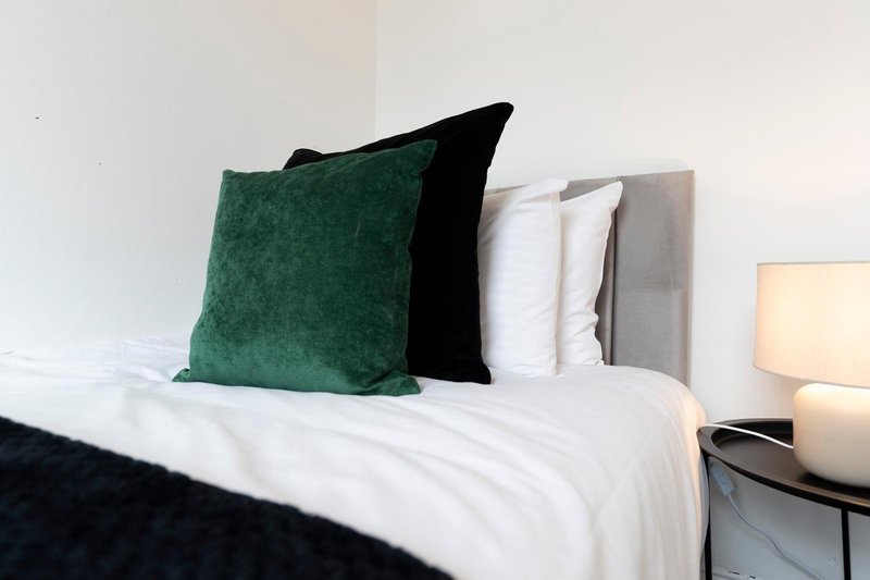 Bed with white bedding, green and black decorative pillows, and bedside lamp