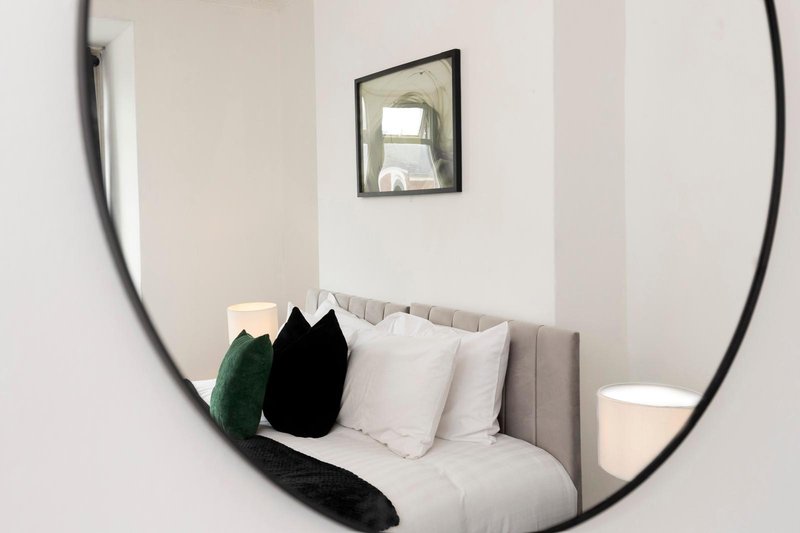Modern bedroom nook with grey upholstered chair, cushions, and round mirror on white wall
