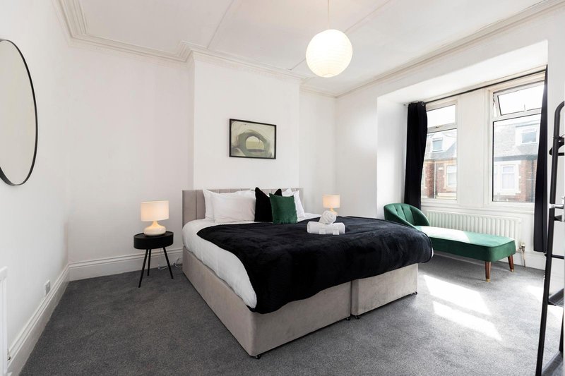 Spacious modern bedroom with double bed, green accent chair, round mirror and pendant lighting