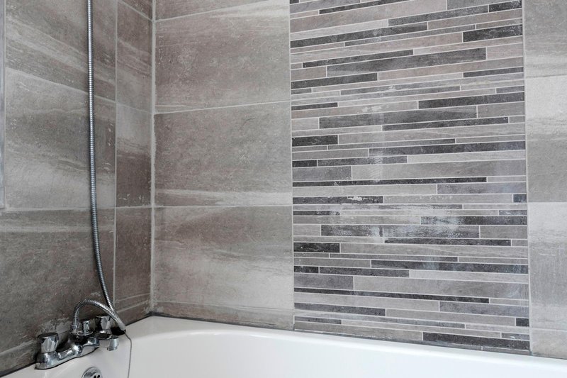 Modern bathroom with tiled shower enclosure, grey and white mosaic wall tiles, white bathtub