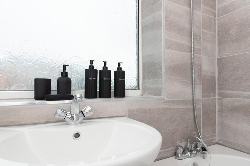 Modern bathroom with white round sink, black toiletries bottles, and frosted window overlooking garden