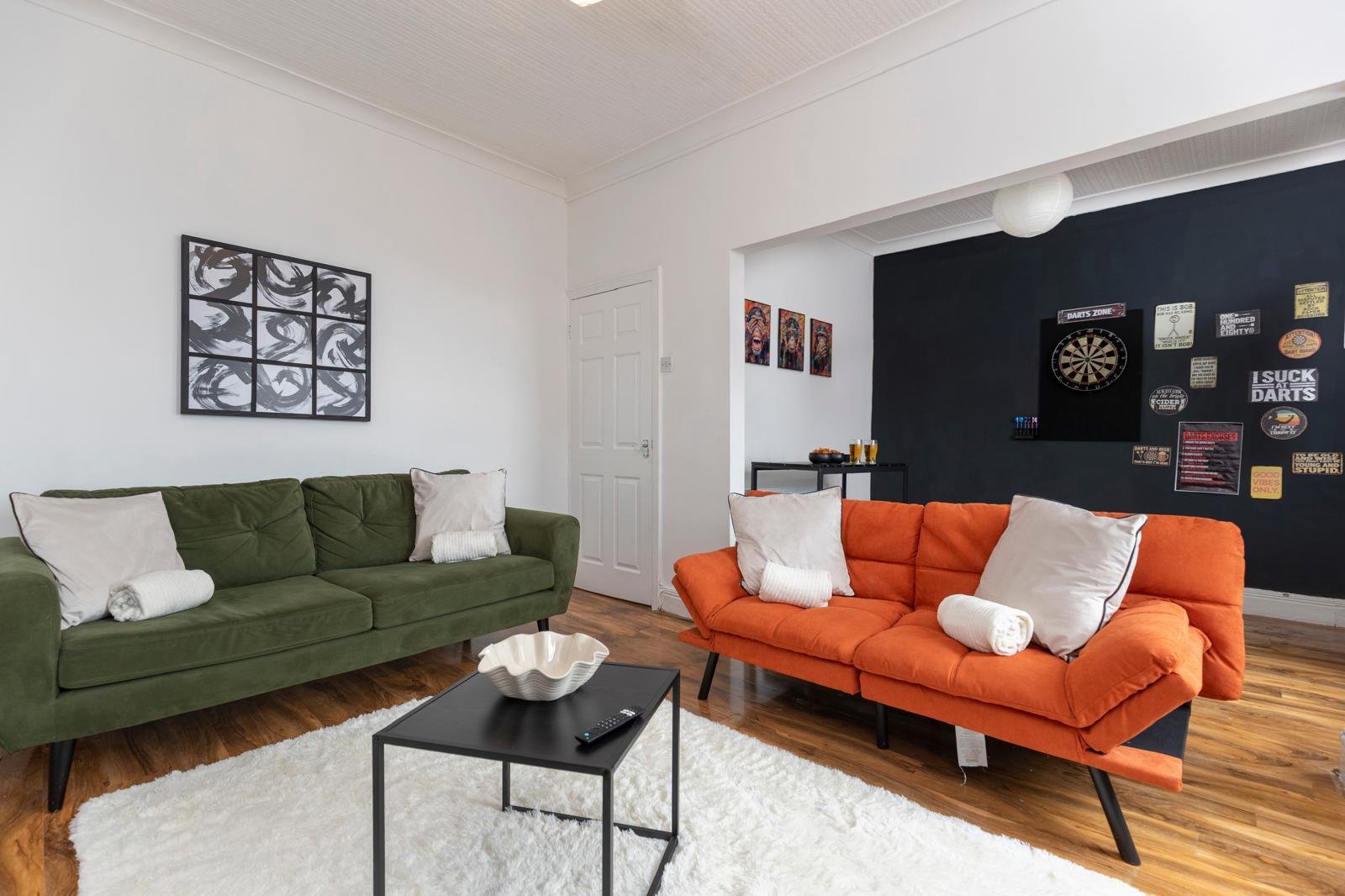 Modern living room with green and orange sofas, black coffee table, and dark accent wall with decor