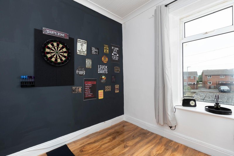 Recreation room with dartboard, wooden flooring, dark accent wall and window overlooking street