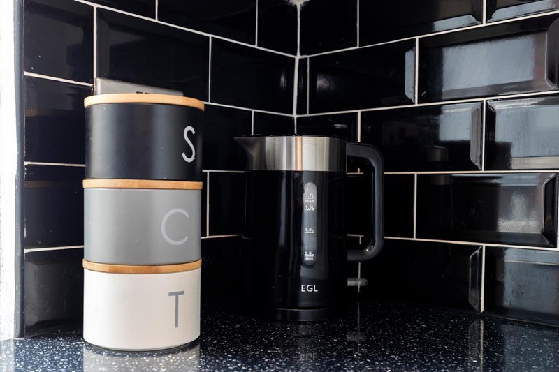 Kitchen counter with black subway tile backsplash, stacked storage containers, and electric kettle