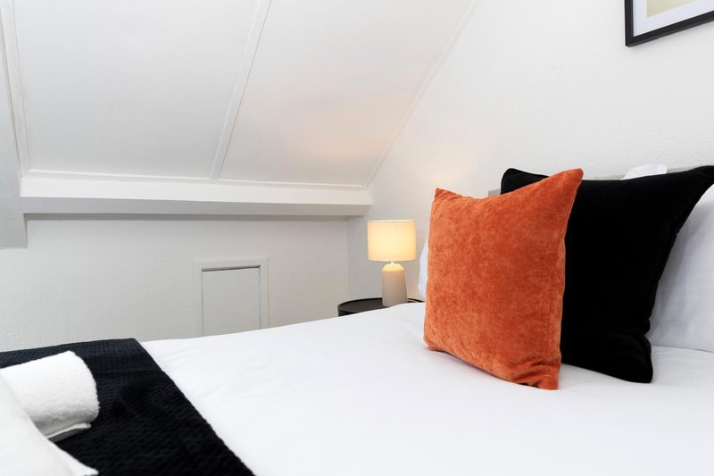 Modern bedroom with white bedding, orange and black decorative pillows, bedside lamp