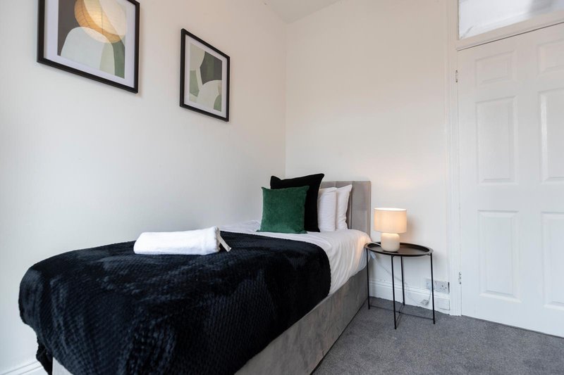 Bedroom with gray bed, black throw, green cushion, bedside table and framed wall art