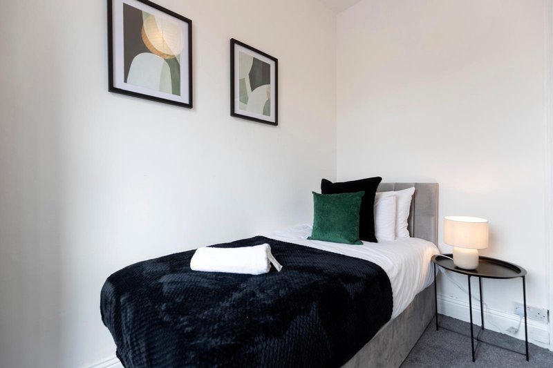 Modern bedroom with double bed, dark blanket, green and white pillows, bedside table and framed wall art