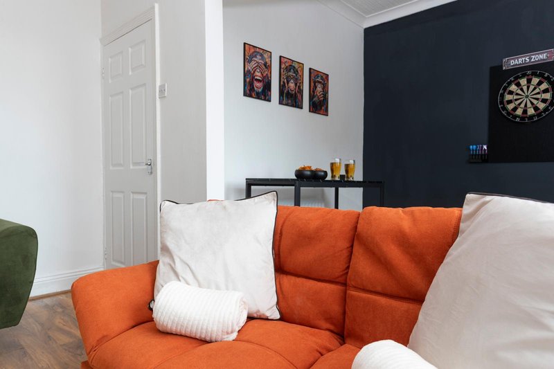 Living room with orange sofa, white cushions, dark feature wall and dartboard