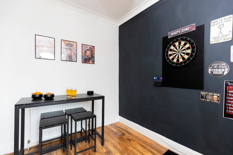 Recreation room with dartboard, bar table, stools, framed wall art and dark feature wall