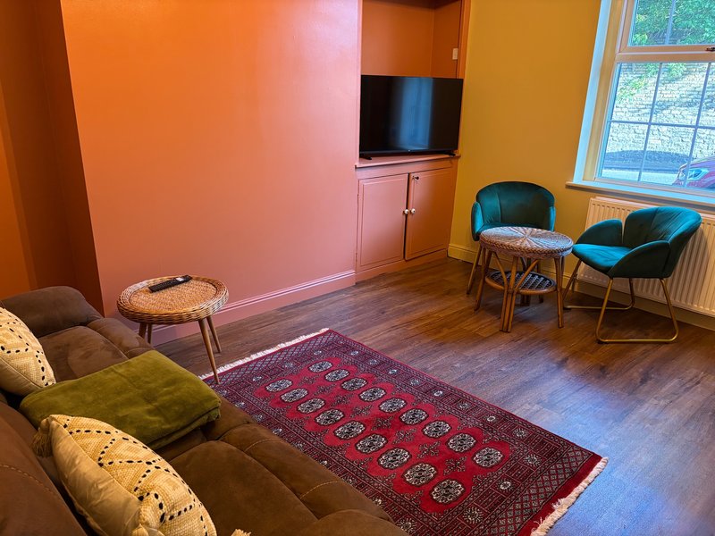 Colourful living room with sofa, chairs, wooden floor, TV and large windows