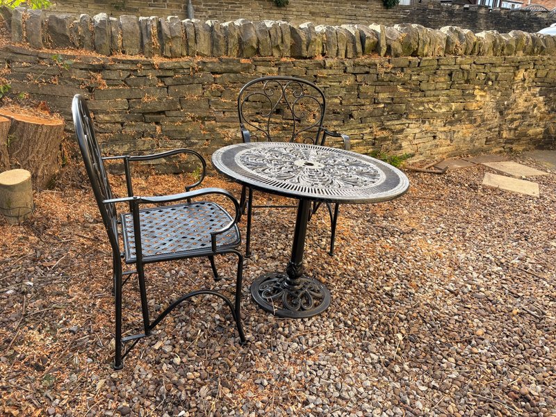 Outdoor seating area with metal bistro table and chairs against stone wall