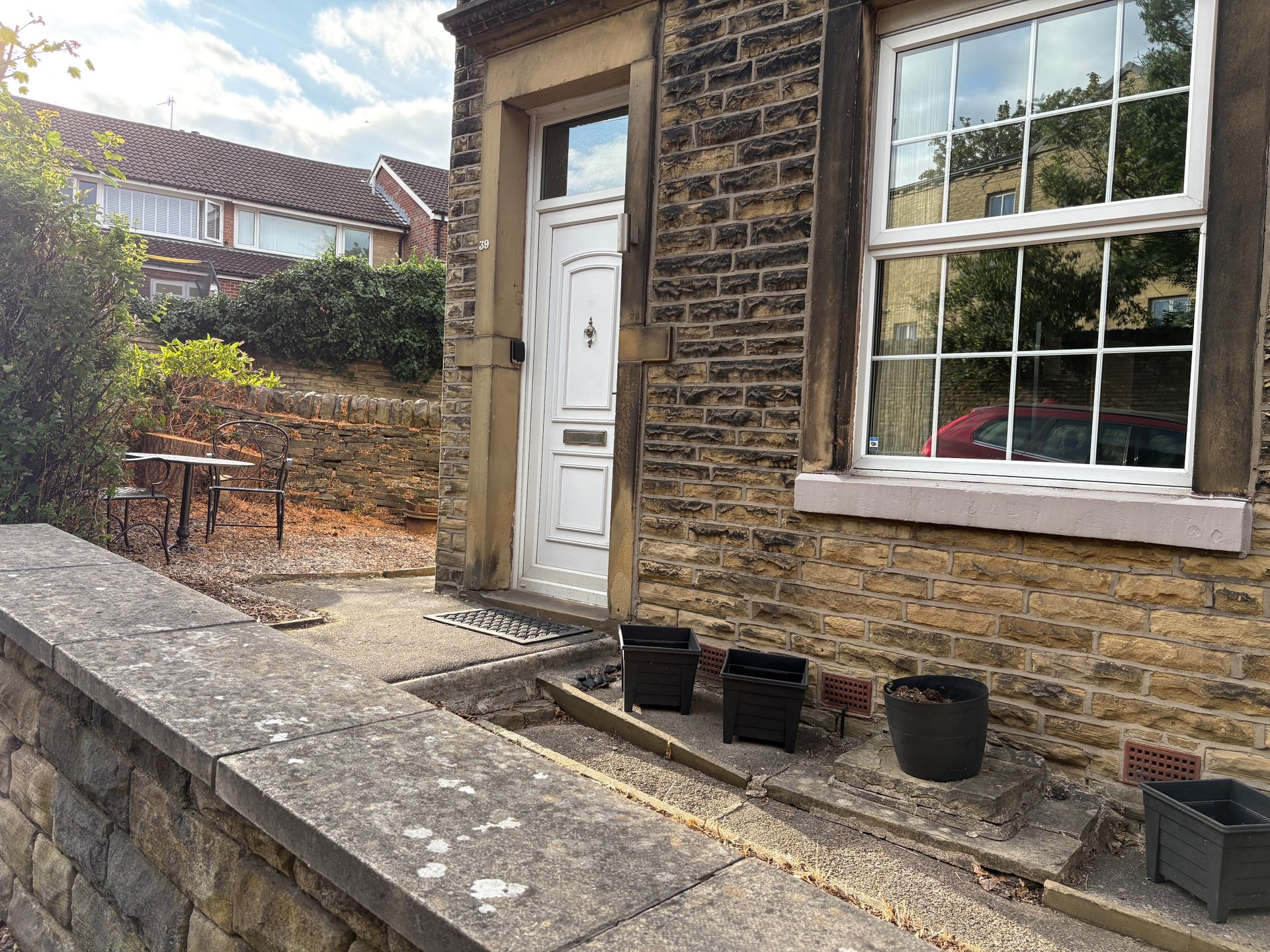 Stone cottage exterior with white door, window, paved courtyard and garden area