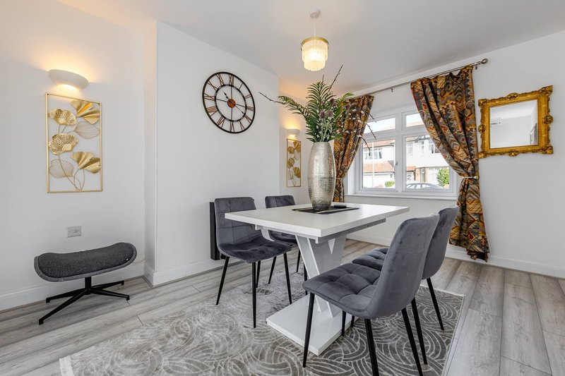 Modern dining room with white table, grey chairs, wall clock, and gold-framed artwork