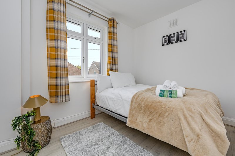 Bright bedroom with single bed, yellow checked curtains, window view and potted plant