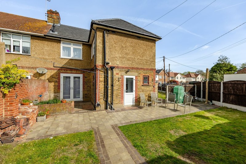 Semi-detached brick house with patio, garden, and side extension under clear sky