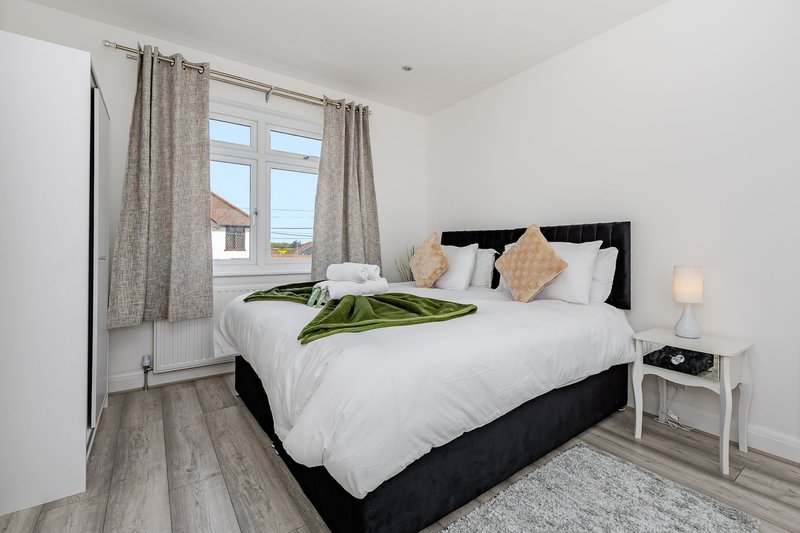 Bright bedroom with double bed, black headboard, white bedding, and window with grey curtains