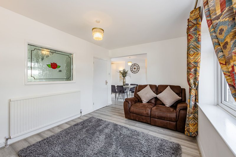 Bright living room with brown leather sofa, gray rug, framed artwork and patterned curtains