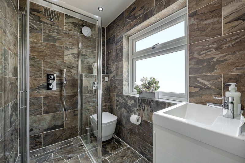 Modern bathroom with walk-in shower, white sink, toilet, and window with natural light