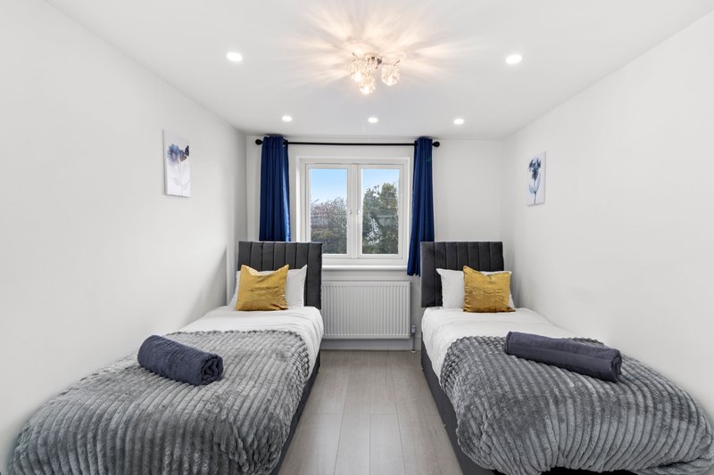 Twin bedroom with two single beds, navy bedding, yellow pillows, and window with blue curtains