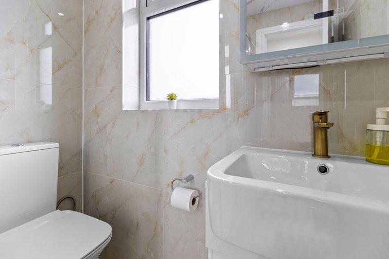 Modern bathroom with white toilet, curved sink, marble-effect tiles and window