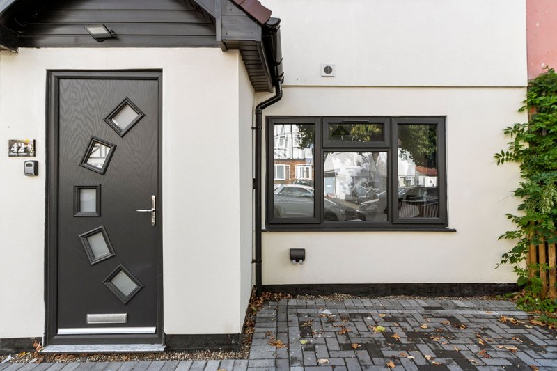 Modern house exterior with dark front door, window, paved driveway and ivy-covered wall