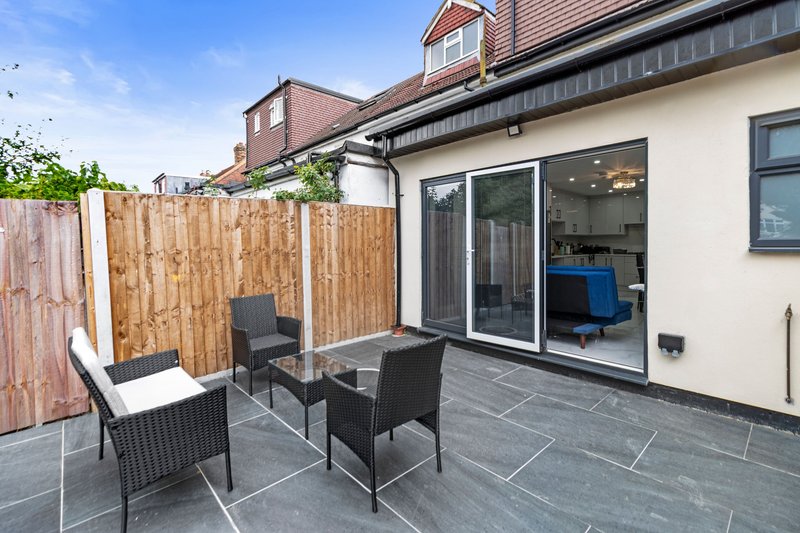 Modern patio with black wicker chairs, table, wooden fence and patio doors