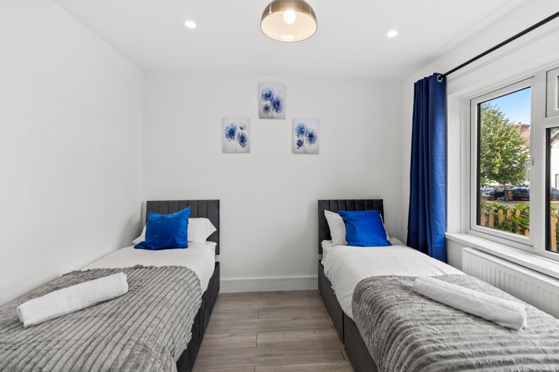 Twin bedroom with two single beds, blue cushions, white walls and large window with garden view