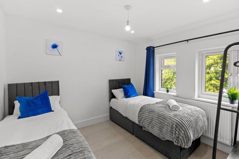 Bright twin bedroom with two single beds, blue cushions, grey upholstery and windows overlooking garden