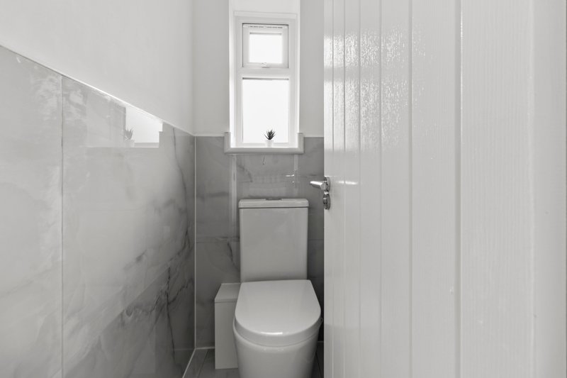Compact bathroom with white toilet, gray tile walls, and small window