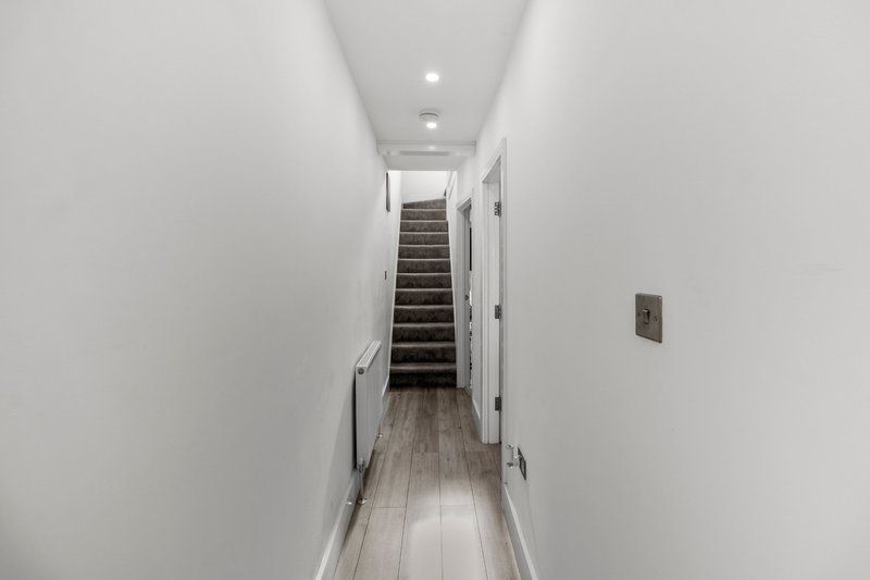 Narrow hallway with wooden floor, white walls, and staircase leading upward