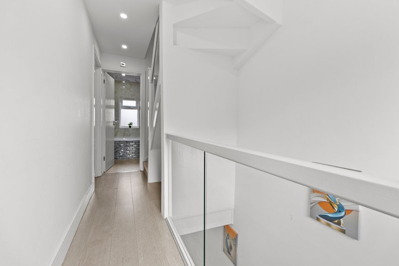Bright modern hallway with wooden flooring, white walls, glass railing and recessed lighting