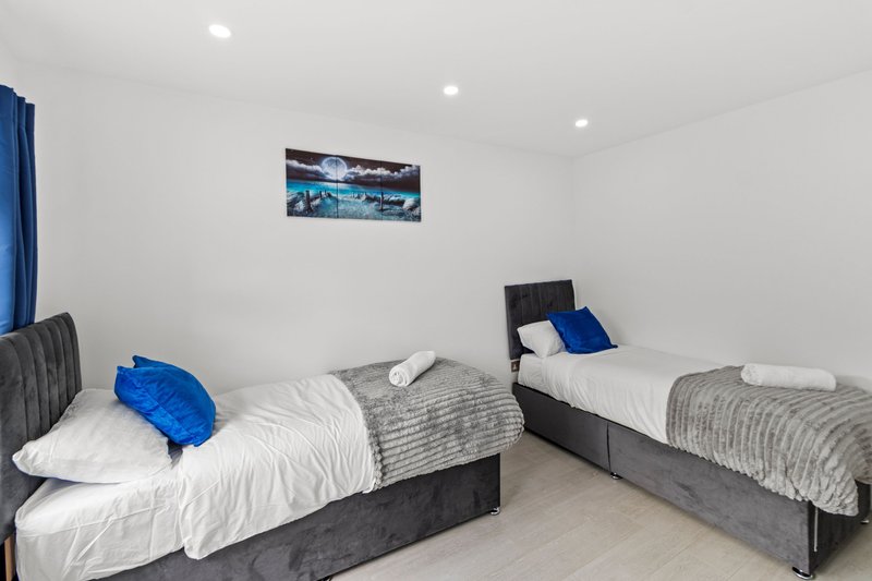 Twin bedroom with two single beds, white bedding, blue pillows and wall-mounted landscape artwork