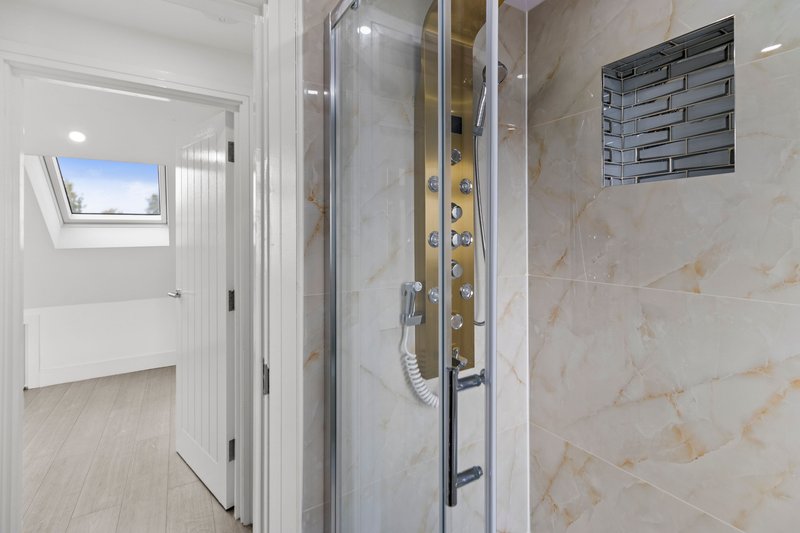 Modern bathroom with walk-in shower enclosure, beige tile walls, and skylight window