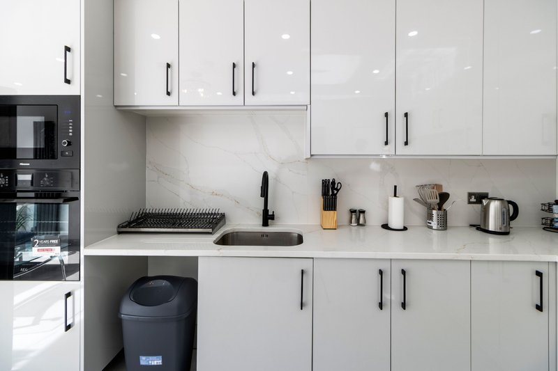 Modern white kitchen with marble countertop, built-in appliances, and open shelving with utensils