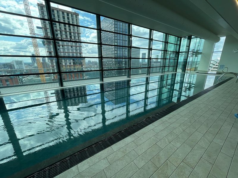 Indoor swimming pool with floor-to-ceiling windows overlooking city skyline and tall buildings