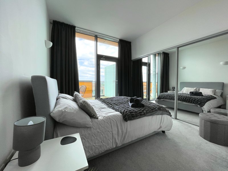 Modern bedroom with double bed, mirrored wardrobe, dark curtains and patio doors