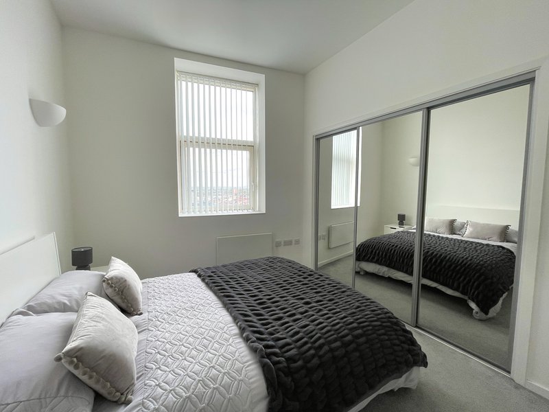 Modern bedroom with double bed, white pillows, dark quilted bedding, mirrored wardrobe and window