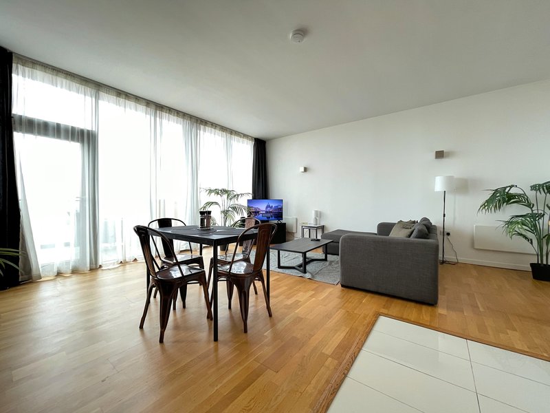 Open-plan living room with dining table, sofa, wooden flooring and large windows