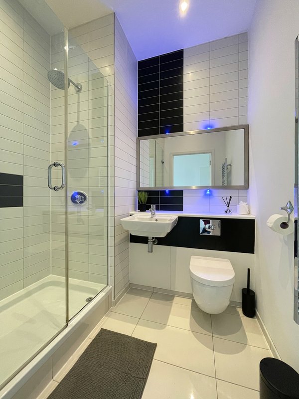 Modern bathroom with walk-in shower, white tile walls, black vanity, mirror and toilet