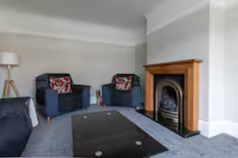 Living room with two navy armchairs, fireplace, wooden mantelpiece, and dark floor