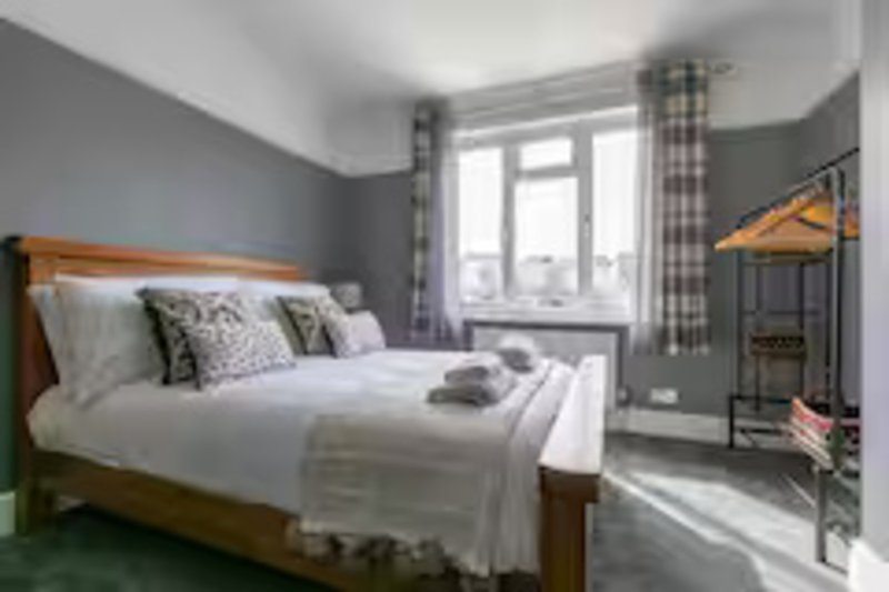 Modern bedroom with wooden bed frame, white bedding, grey walls, and ensuite shower room visible