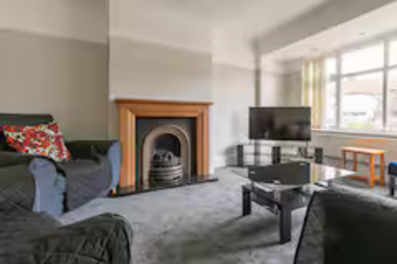 Spacious living room with fireplace, sofa, TV, and large windows overlooking garden