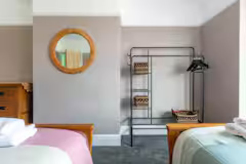 Bedroom with two single beds, wooden frame, round mirror, and metal clothing rack