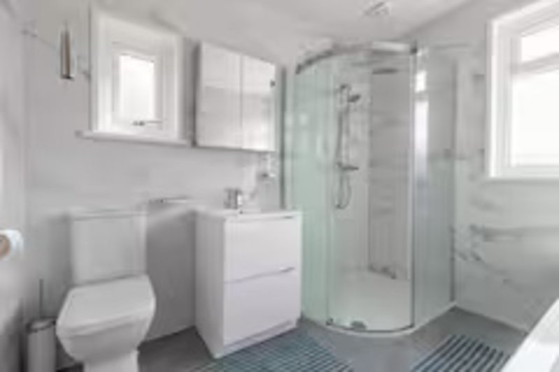 Modern bathroom with white vanity, toilet, curved shower enclosure and blue floor tiles