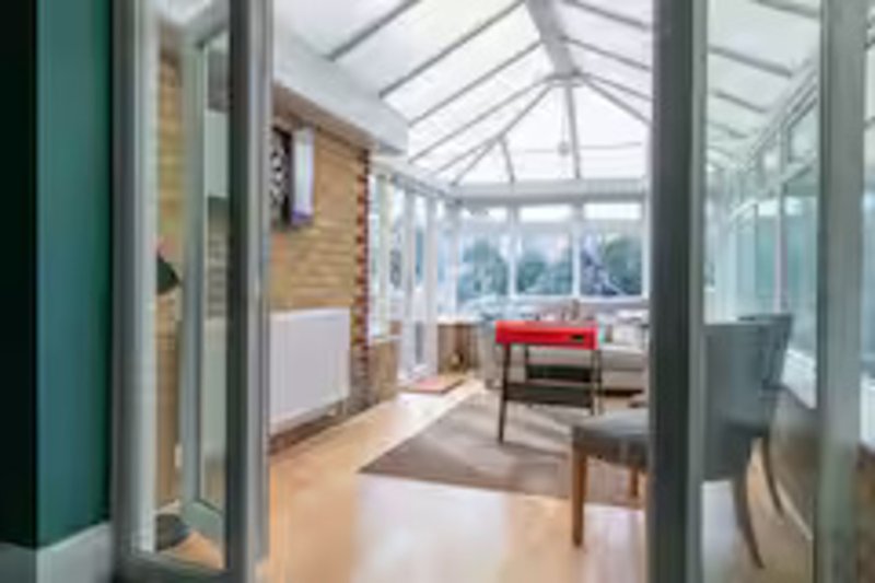 Modern conservatory with glass roof, red chair, wooden wall paneling and natural light