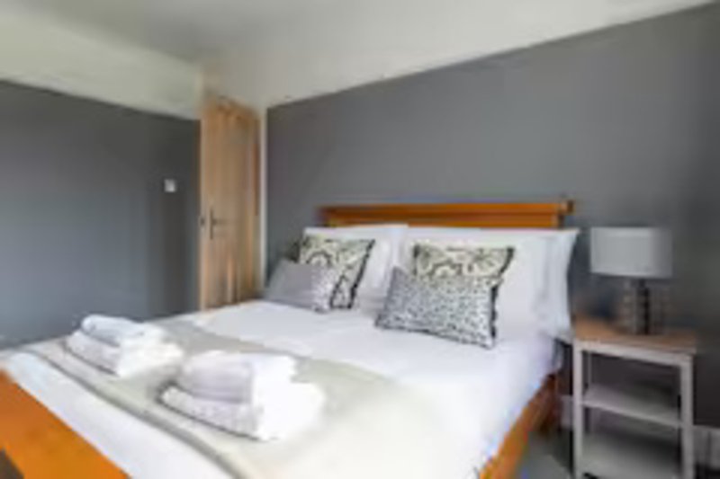 Modern bedroom with double bed, wooden headboard, grey walls, and white bedside table