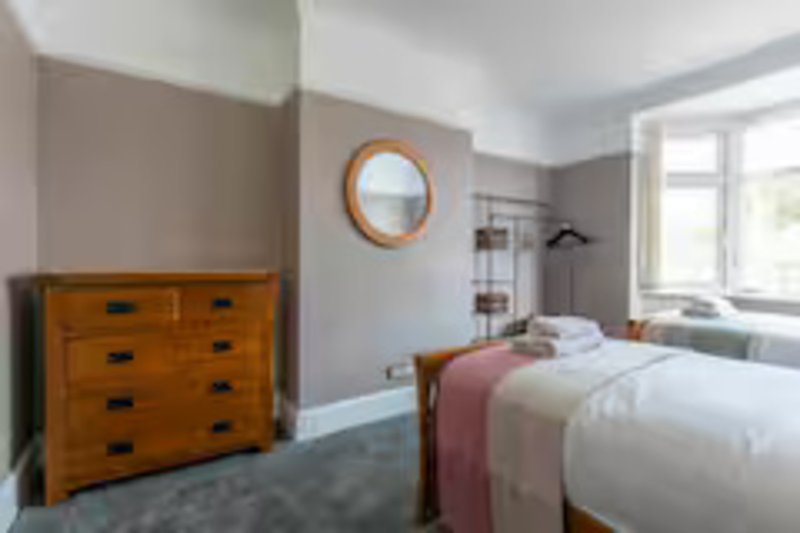 Bright bedroom with double bed, wooden dresser, round mirror, and large windows