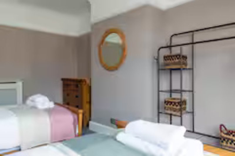 Twin bedroom with white bedding, pink throw, wooden furniture and wall mirror