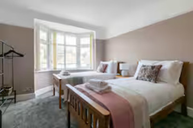 Bright modern bedroom with two beds, bay window, grey carpet and neutral walls