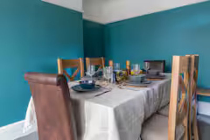 Dining area with turquoise walls, white tablecloth, wooden chairs, and place settings
